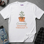 Text "Currently Growing Through It" with green plant growing in a broken terra cotta pot.